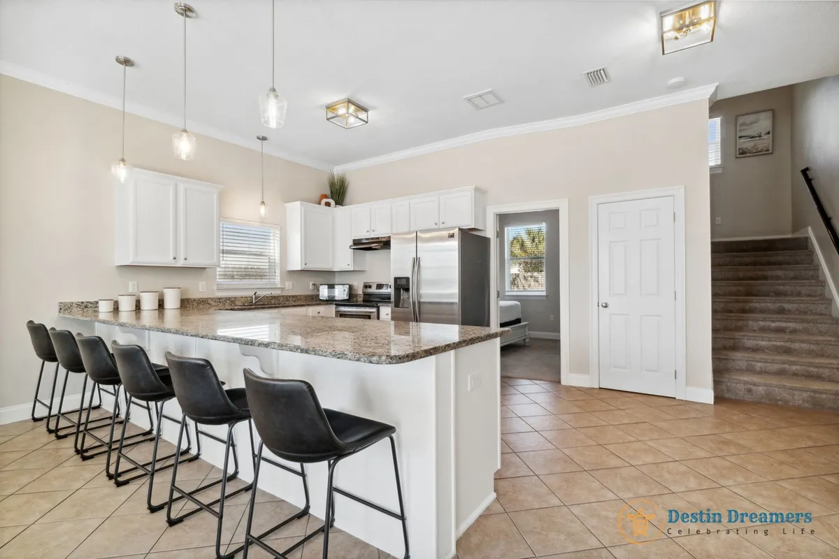 A modern kitchen featuring a granite countertop peninsula with bar stools, stainless steel appliances, and stylish cabinetry. The setup is ideal for casual breakfasts, coffee mornings, or meal prep with friends and family nearby.