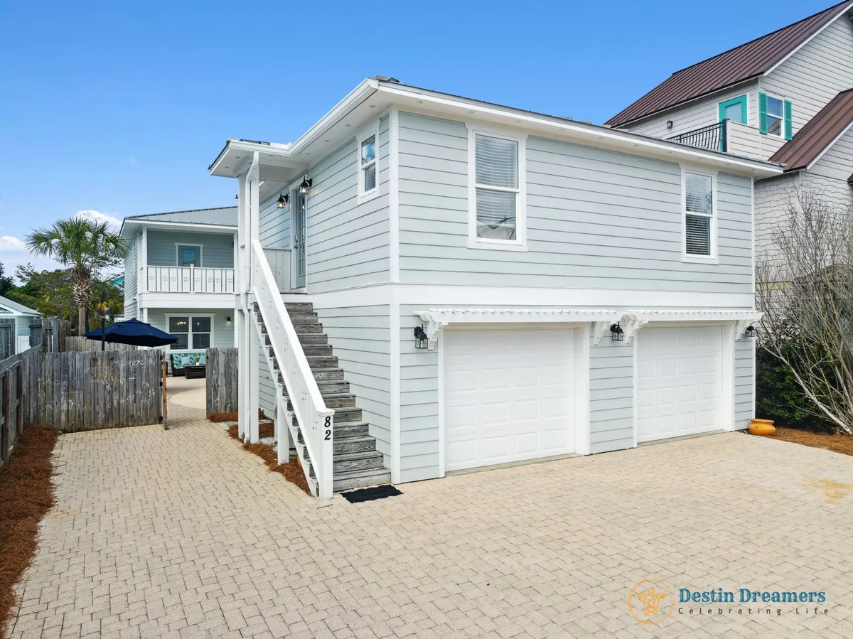 This image showcases the exterior of the property, featuring the main and carriage house structures, a prominent staircase to the upper level, two garage doors, and a spacious paved driveway. The welcoming yard provides space for kids to play and families to gather, perfectly illustrating the multi-generational setup described in the section.