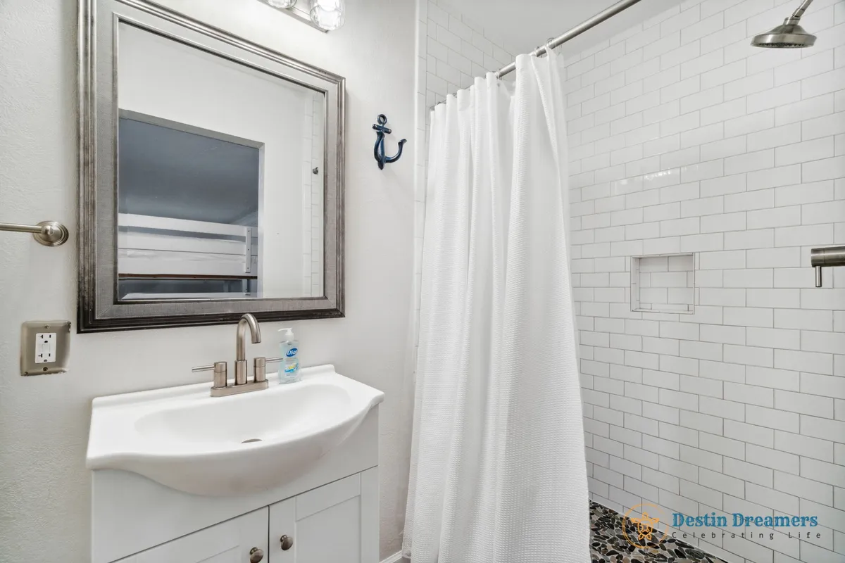 A modern en-suite bathroom featuring a sleek sink with a contemporary faucet, a framed mirror, and a shower area with a crisp white curtain. The space is bright and inviting, ideal for refreshing routines and self-care rituals.