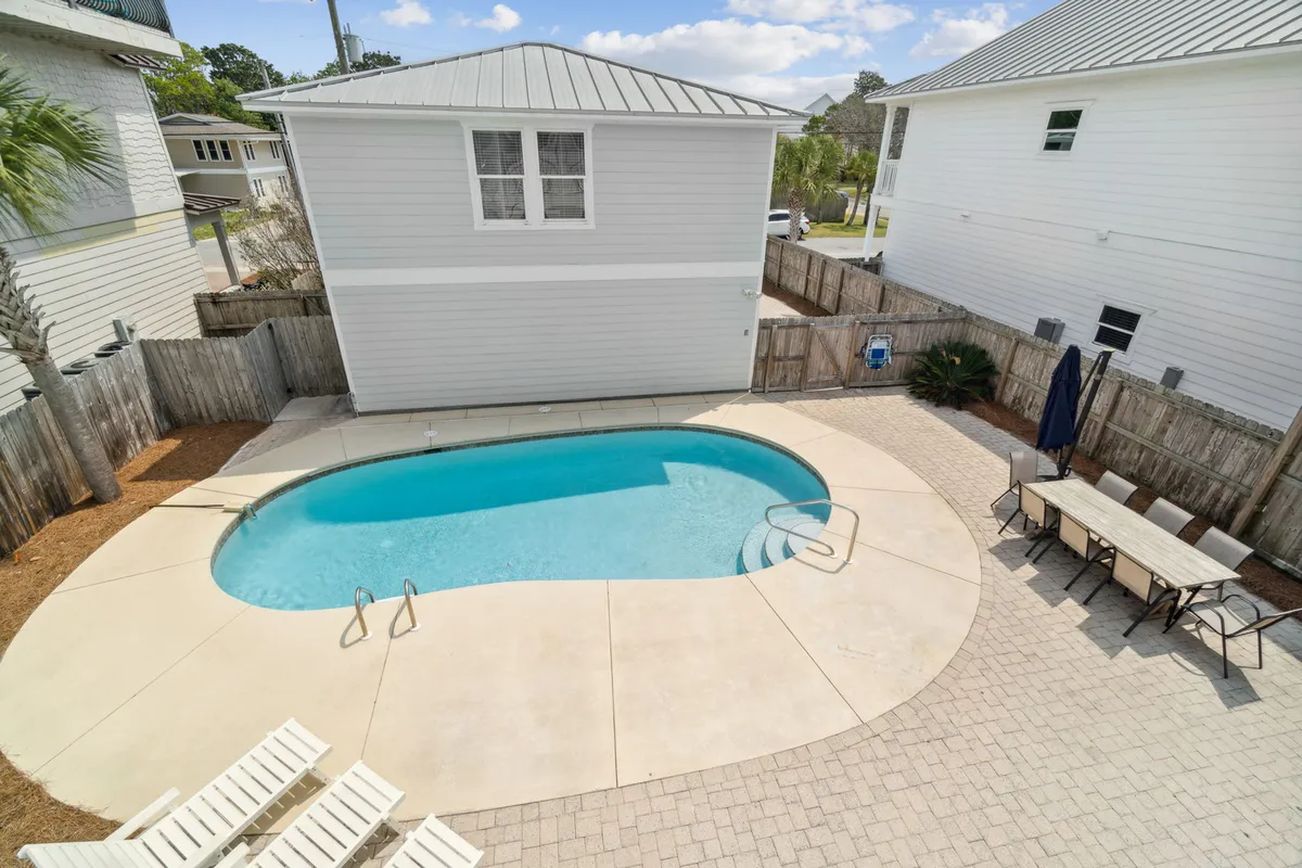 A vibrant exterior shot featuring a sparkling swimming pool surrounded by a landscaped yard, with outdoor seating arranged for relaxation and socializing. The scene is lit with natural sunlight, creating an inviting atmosphere for both swimming and lounging. The lush greenery adds to the feeling of a private oasis.