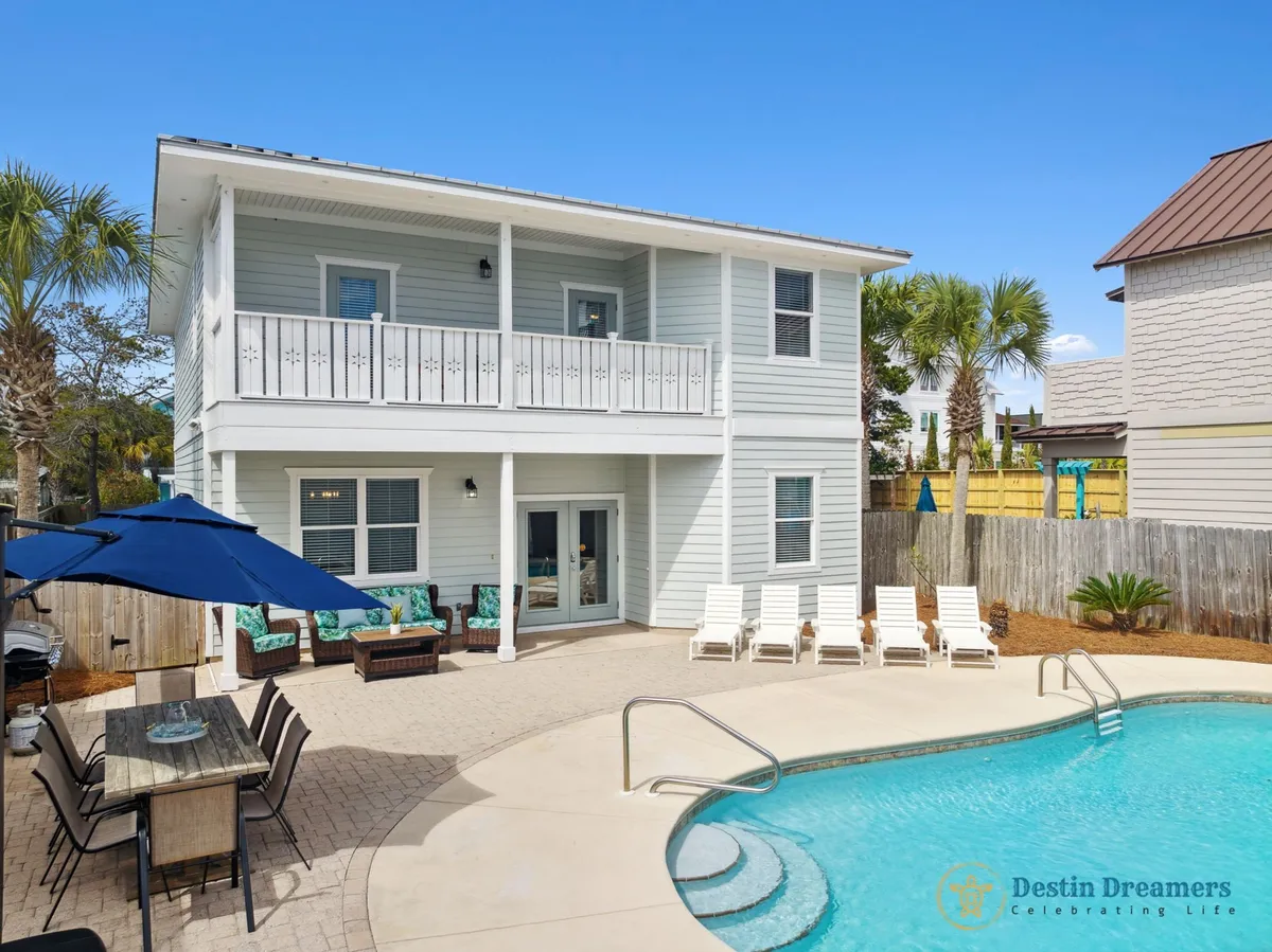 The image showcases a private heated pool with gentle steps and a handrail, surrounded by a sun-kissed patio featuring a shaded dining area with umbrella and chairs, inviting lounge seating with plush cushions, and an upstairs balcony overlooking the tranquil courtyard. The scene exudes relaxation and togetherness, with ample space for swimming, outdoor dining, and sunset views.
