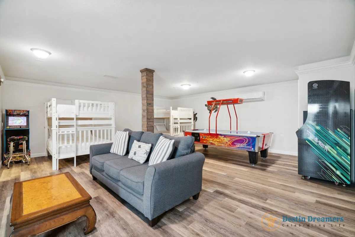 The image shows a vibrant game room featuring an air hockey table, arcade game machine, bunk beds for kids, and a comfortable sofa. The space exudes energy and fun, with playful decor and plenty of room for both play and relaxation.