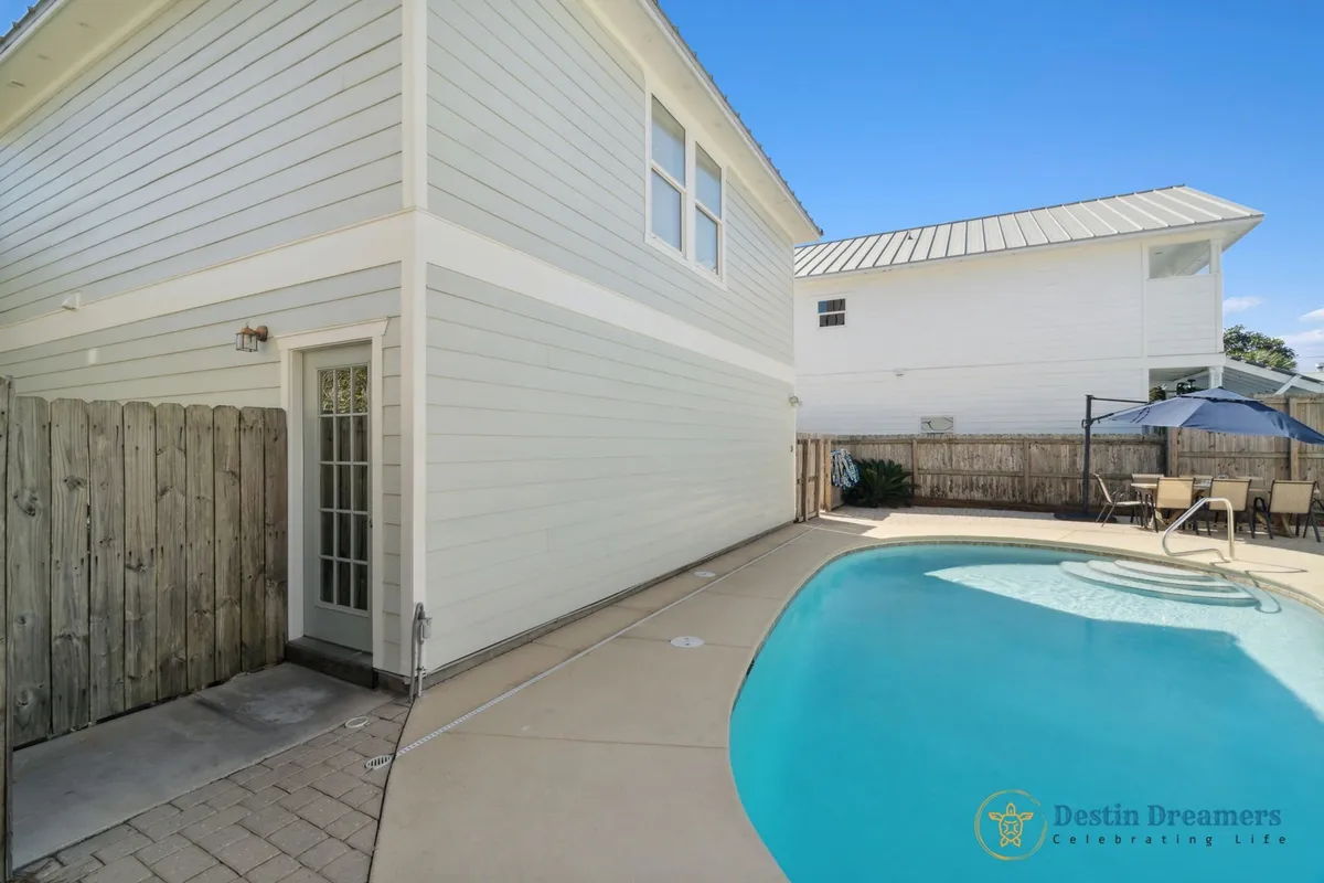 This exterior view highlights the private heated pool, a second floor balcony, a patio dining area with umbrella, and a wooden privacy fence. The arrangement is ideal for both sunbathing and al fresco dining, with the balcony offering an elevated perspective for relaxation or socializing.