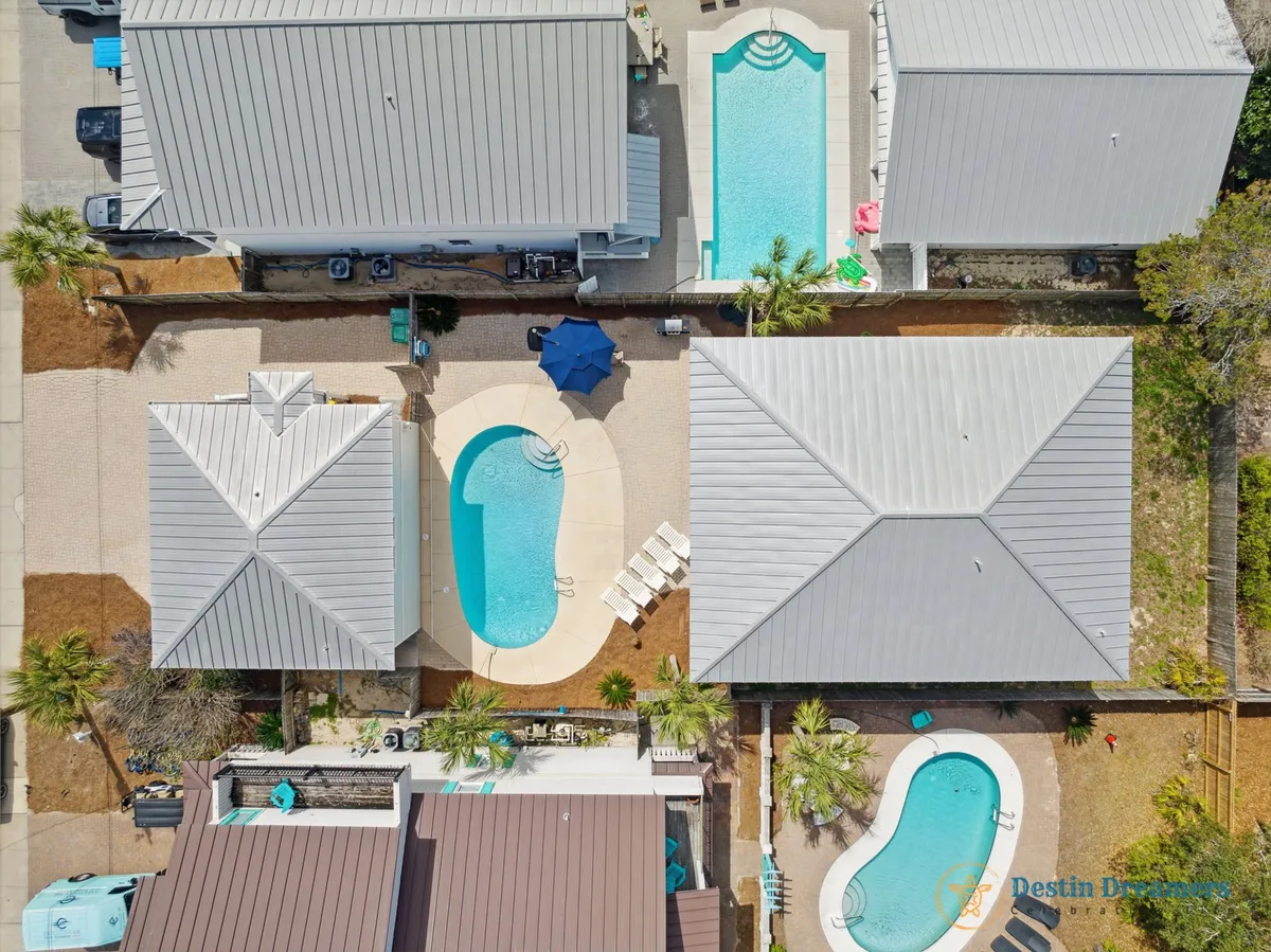 An exterior view featuring three distinct private pools, surrounded by well-maintained patios, outdoor seating, umbrellas, and multiple residential buildings with metal roofs. It conveys the sense of exclusivity, leisure, and group-friendly amenities that persist regardless of the season.